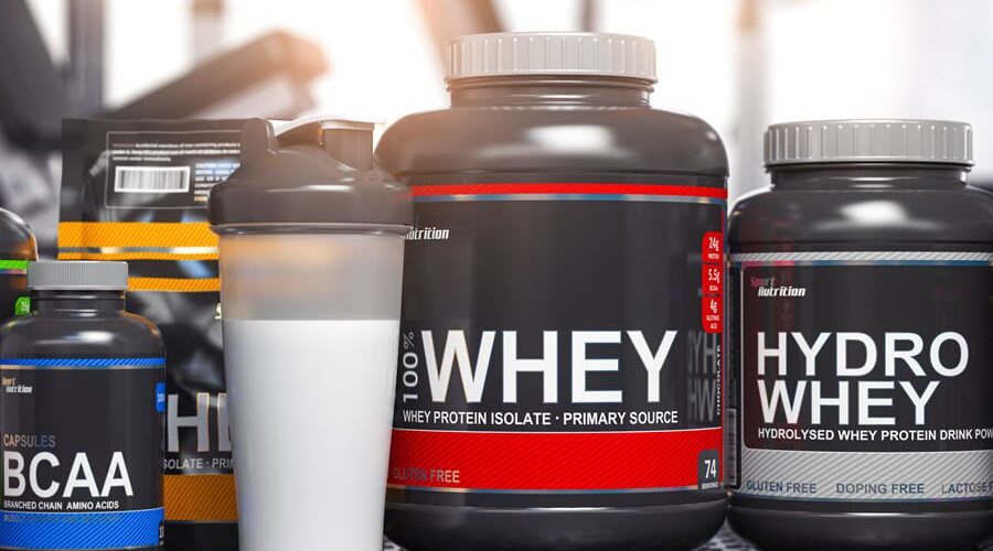 Lactose free bodybuilding supplements including whey protein isolate, hydro whey, and BCAA capsules displayed with protein shaker in gym setting