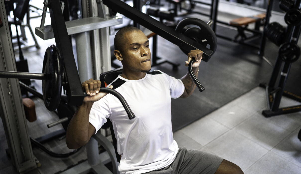 Man performing hypertrophy training chest press exercise on machine in gym demonstrating proper form and controlled movement
