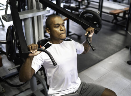 Man performing hypertrophy training chest press exercise on machine in gym demonstrating proper form and controlled movement