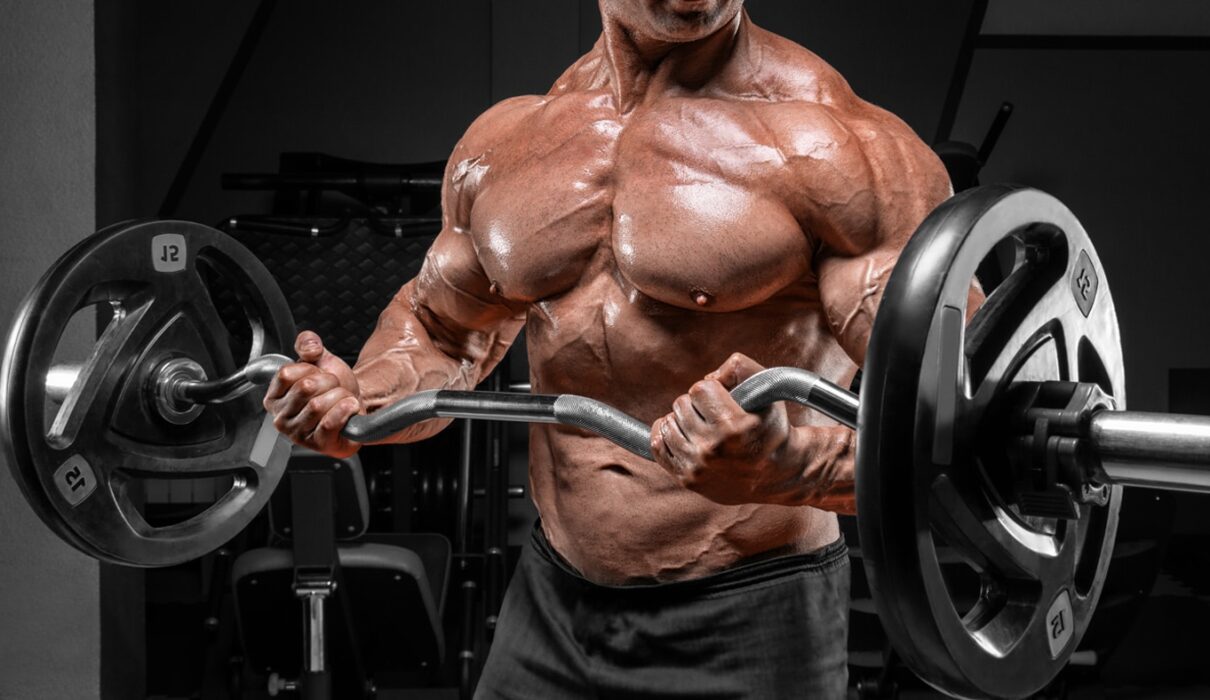 Muscular man performing barbell curls in a gym, highlighting defined chest, arm, and shoulder muscles to demonstrate optimal reps for hypertrophy.