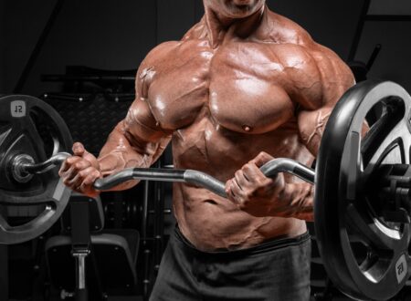 Muscular man performing barbell curls in a gym, highlighting defined chest, arm, and shoulder muscles to demonstrate optimal reps for hypertrophy.