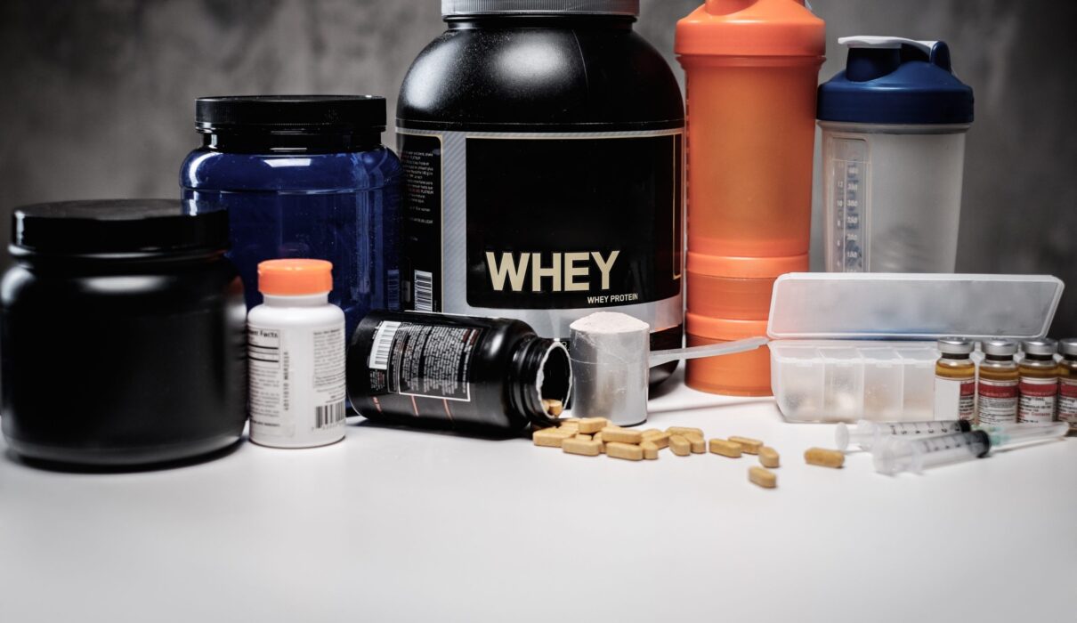 Bodybuilding recovery supplements including whey protein, tablets, capsules, syringes, and shaker bottles arranged on a fitness nutrition setup.