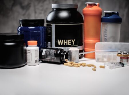 Bodybuilding recovery supplements including whey protein, tablets, capsules, syringes, and shaker bottles arranged on a fitness nutrition setup.