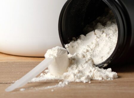 Creatine for muscle gain powder spilling from black container with measuring scoop on wooden surface