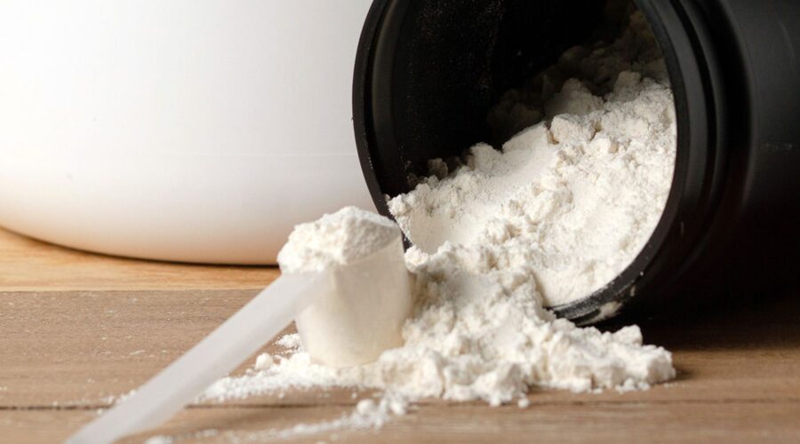 Creatine for muscle gain powder spilling from black container with measuring scoop on wooden surface